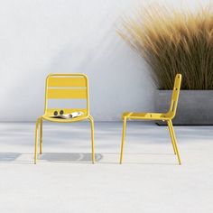 two yellow chairs sitting next to each other in front of a white wall and grass