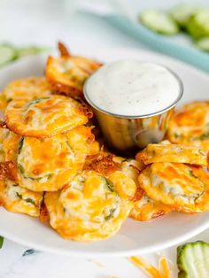 a white plate topped with cheesy pastries next to a bowl of ranch dressing