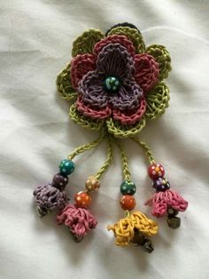 a crocheted flower with beads hanging from it's center on a white sheet