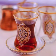 four glass cups with gold rims and designs on the inside are sitting on a white table