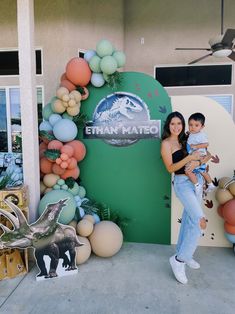 a woman holding a baby standing in front of a sign with balloons and animals on it