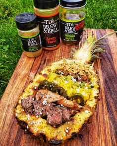 a pineapple with meat and vegetables on it next to jars of bbq rubs