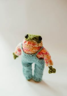 a small stuffed frog wearing a sweater and scarf