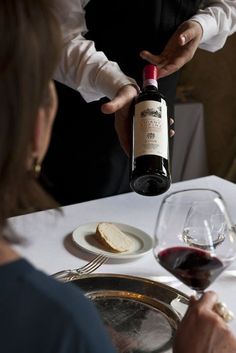 a man pouring red wine into a glass at a table with bread and wine glasses