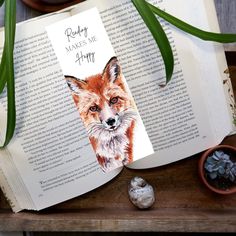 an open book sitting on top of a wooden table next to some rocks and plants