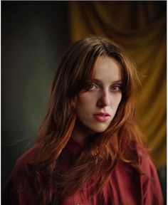 a woman with long red hair is looking at the camera while wearing a red shirt