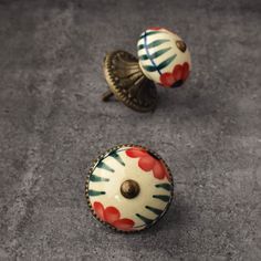 two decorative knobs with red flowers on them sitting on a gray surface next to each other