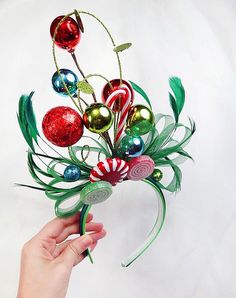 a hand holding a christmas decoration with ornaments on it's head and green stems