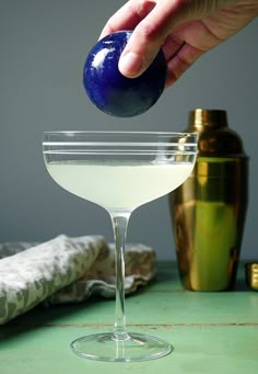 a hand is squeezing an olive into a martini glass with a blue garnish on the rim