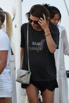 a woman talking on her cell phone while wearing black shorts and a saint laurent t - shirt