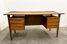 a wooden desk with two drawers sitting on top of cement floor next to a white wall