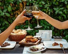 two people toasting with wine at an outdoor dining table set for dinner and desserts