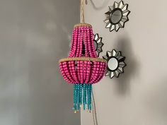 a pink and blue beaded chandelier hanging from a wall next to two mirrors