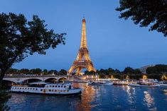 the eiffel tower is lit up at night with boats in the water below