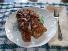 two pieces of meat are on a plate with a fork and napkin next to it