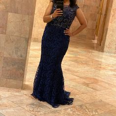 a woman in a blue dress taking a selfie with her cell phone while standing next to a wall