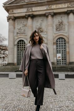 a woman is walking in front of a building with a gray coat over her shoulders