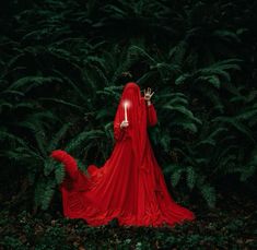 a woman in a red dress is walking through the woods