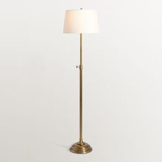 a gold floor lamp with a white shade on the base and a light bulb at the end