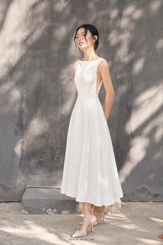 a woman standing in front of a wall wearing a white dress