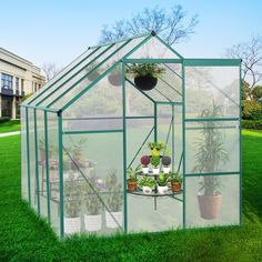 a green house with potted plants inside on the grass in front of a building