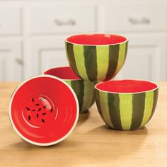 three striped bowls sitting on top of a wooden table next to white cabinets and drawers