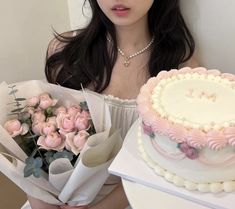 a woman holding a bunch of flowers next to a cake and bouquet of pink roses