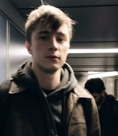 a young man standing in an elevator with his head turned to the side and looking at the camera