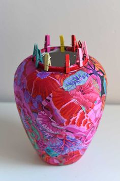 a colorful vase with clothes pins sticking out of it's sides on a white surface