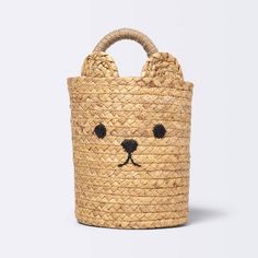 a straw bag with a bear face drawn on the front and sides, sitting in front of a white background