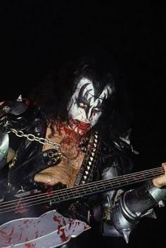 a man dressed in black and white with blood on his face playing a bass guitar