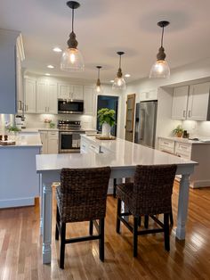 a large kitchen with white cabinets and wooden flooring, along with two bar stools