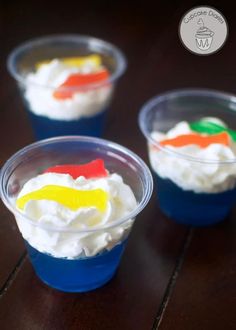 three plastic cups filled with whipped cream and colorful toppings on top of a wooden table