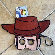 a cardboard mask with a red hat and sunglasses on it's face, sitting on a tile floor