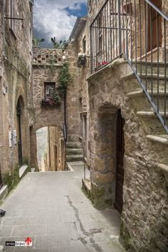 an alley way with stone buildings and steps leading up to the second floor, under a cloudy blue sky