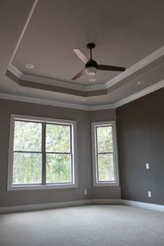 an empty room with two windows and a ceiling fan in the middle of the room