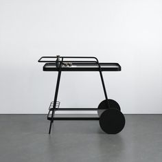 a black cart sitting on top of a cement floor next to a white wall with an object hanging from it's side