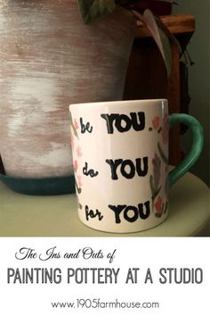 a coffee cup sitting on top of a table next to a potted plant with the words, be you as if you're painting pottery at a studio