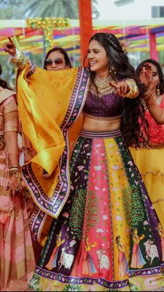 a group of women standing around each other wearing colorful outfits and holding hands in the air