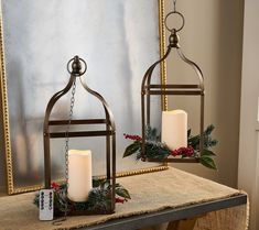 two lit candles sitting on top of a table next to a mirror and christmas decorations