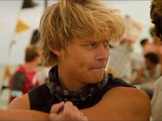 a man with blonde hair wearing a bandana and looking off to the side while standing next to another man