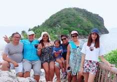 a group of people sitting on top of a wooden bench next to the ocean with an island in the background