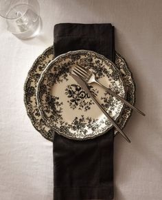 a table setting with black and white plates, silverware and wine glasses on it