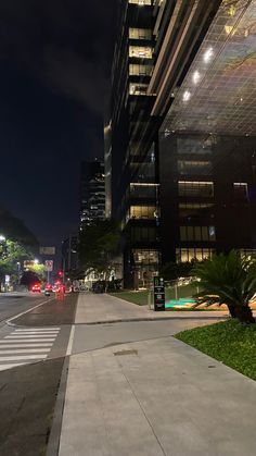 an empty city street at night with tall buildings in the back ground and lights on