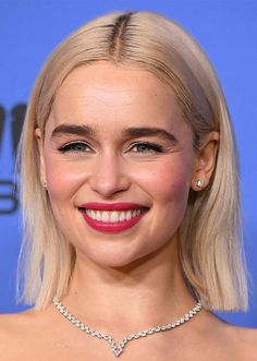 a woman with blonde hair wearing a diamond necklace and smiling at the camera while standing in front of a blue background