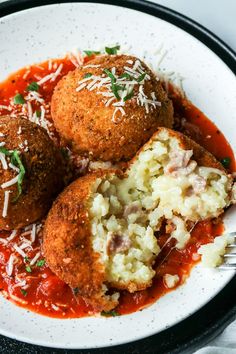 three meatballs covered in marinara sauce and parmesan cheese on a plate with a fork