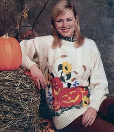 a woman sitting on hay next to a pumpkin