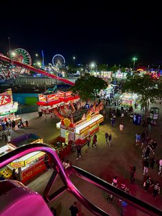 an aerial view of a fair at night with people walking around and carnival rides in the background