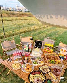 a table full of food sitting on top of a grass covered field next to a boat