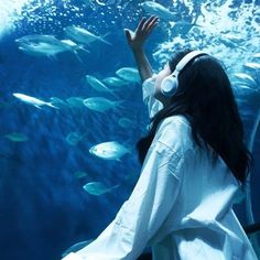 a woman wearing headphones is looking at fish in an aquarium with her hands up